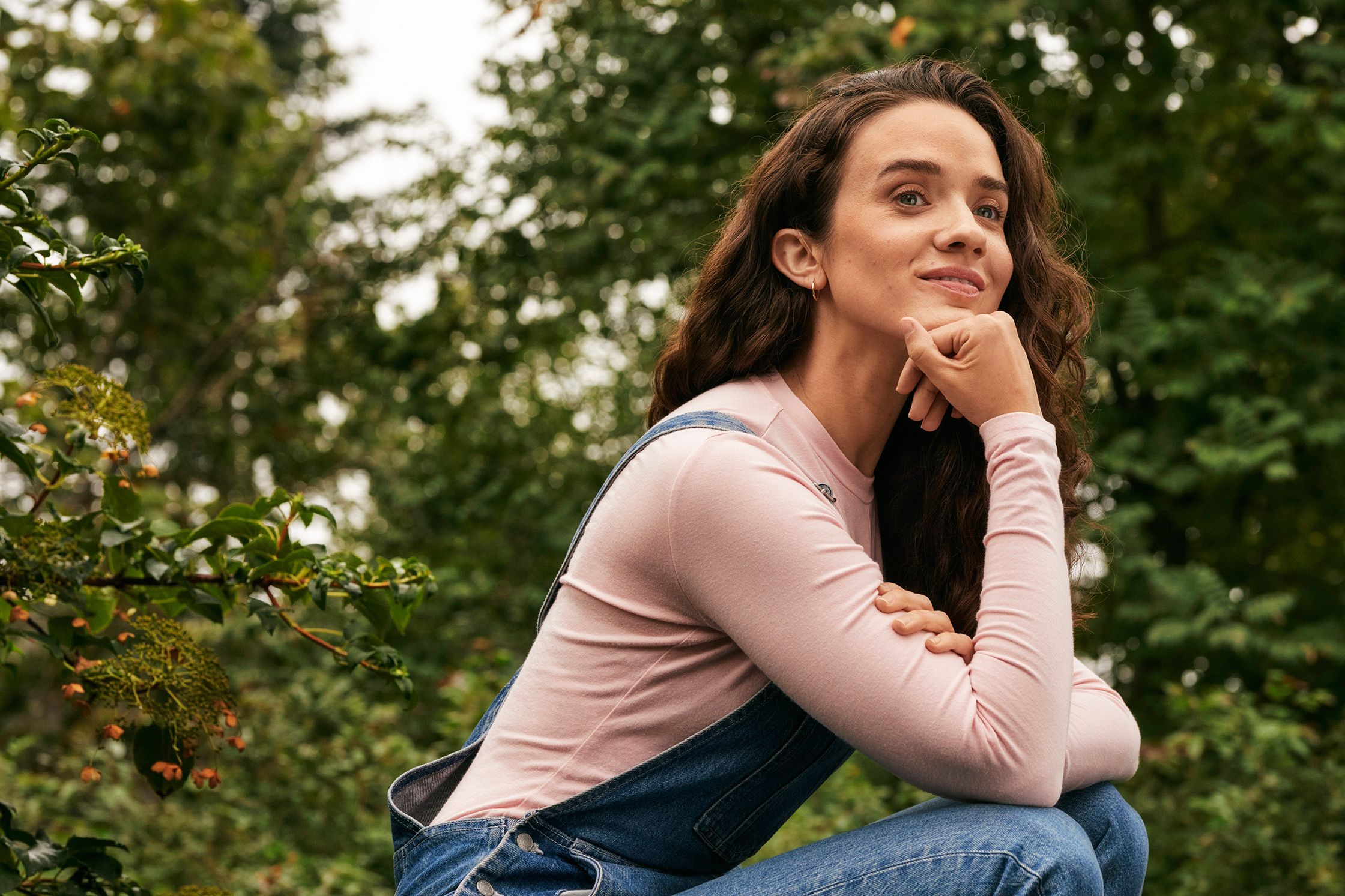 Mørkhåret kvinne med høreapparater foran en bakgrunn av bladrike trekroner