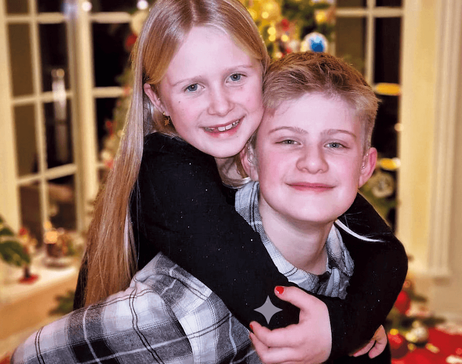 Smilende, lysluggede Aron har den milende og lysluggede søsteren sin, Nora, på ryggen og de poserer foran familiens juletre i stuen.