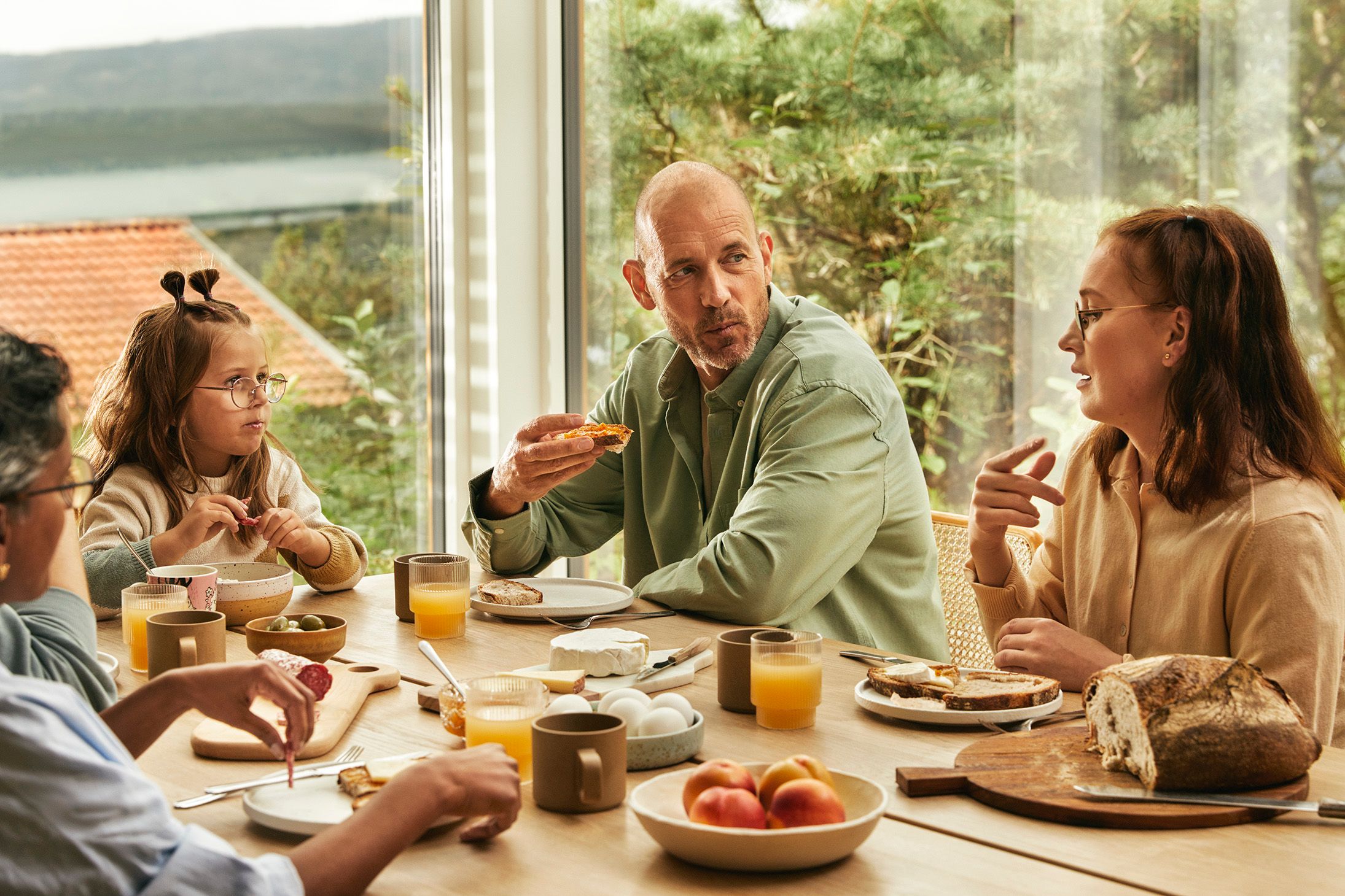 Tre voksne og et barn sitter ved et bord og spiser frokost sammen.