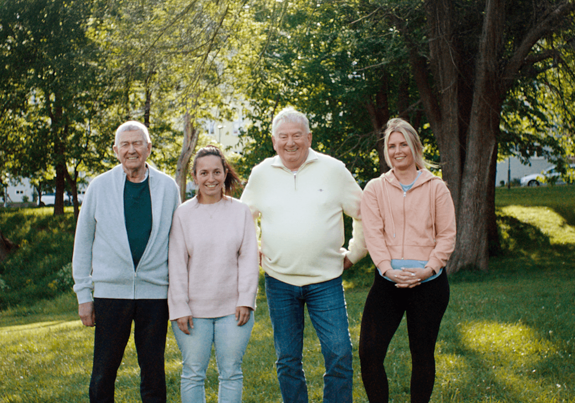 Fire personer står skulder mot skulder og ser smilende inn i kameraet foran grønne trekroner
